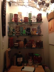 tiki mugs on glass shelves in a small nook with boring white walls